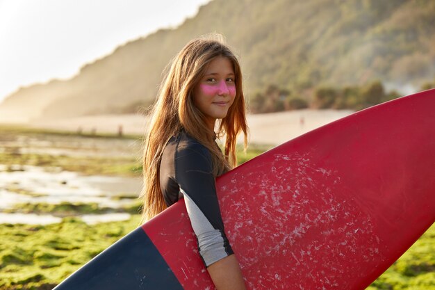 Surfer en oceaan concept. Opgetogen donkerharige vrouw draagt gewaxte surfplank-looks met tevreden uitdrukking