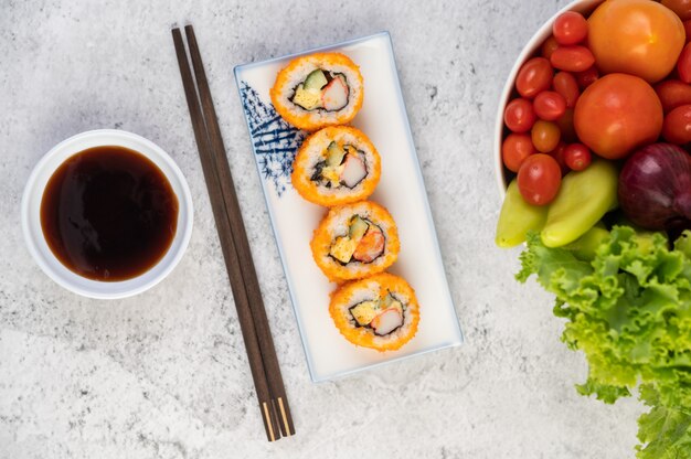 Sushi is in een bord met stokjes en dipsaus op een witte cementvloer.