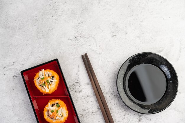 Sushi is in een bord met stokjes en dipsaus op een witte cementvloer.
