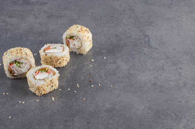 Sushi rolt versierde sesamzaadjes op stenen achtergrond.