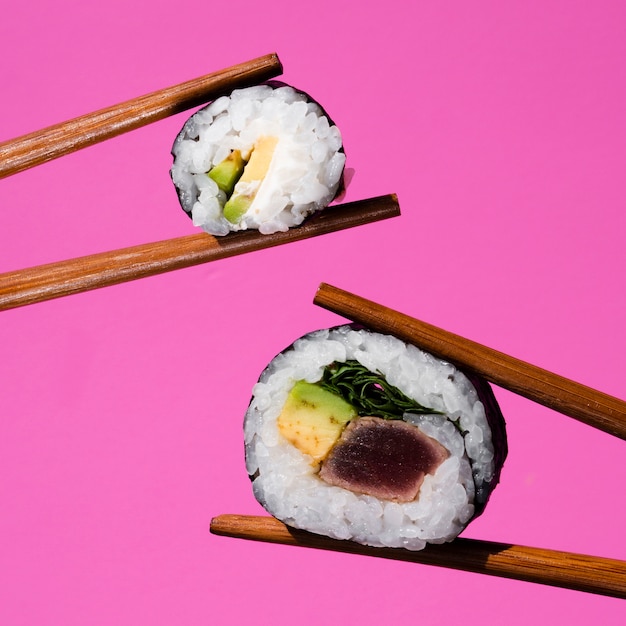 Sushibroodjes holded door eetstokjes op een roze achtergrond