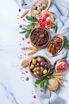 Symbolen van judaic vakantie tu bishvat, rosh hashana nieuwjaar van de bomen. mix van gedroogde vruchten, dadels, vijgen, druiven, gerst, tarwe, olijven, granaatappel op een marmeren tafel. ruimte achtergrond kopiëren