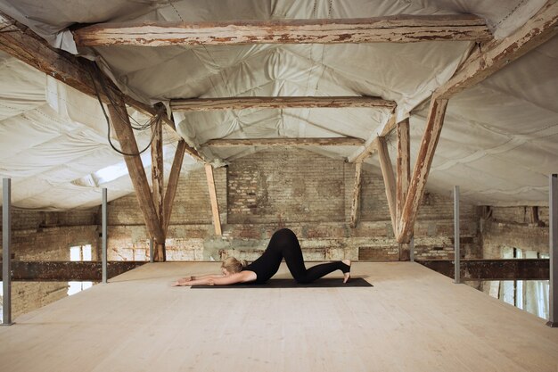 Symmetrie. Een jonge atletische vrouw oefent yoga op een verlaten bouwgebouw. Geestelijke en lichamelijke gezondheid. Concept van een gezonde levensstijl, sport, activiteit, gewichtsverlies, concentratie.