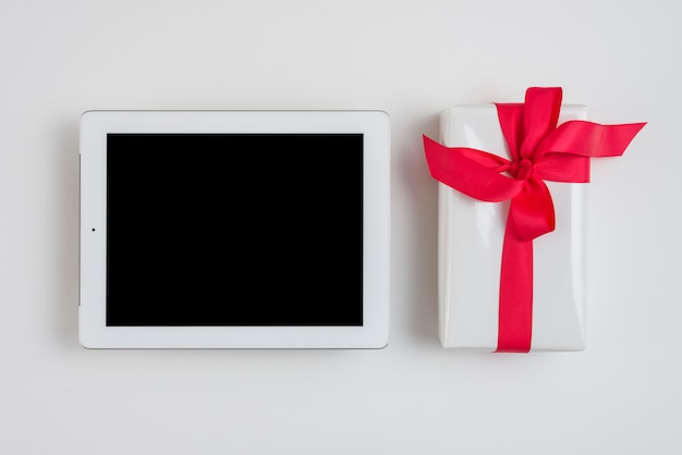 Tablet in de buurt van geschenkdoos met rood lint