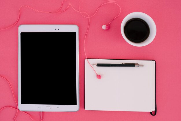 Tablet met oortelefoons dichtbij notitieboekje en koffie