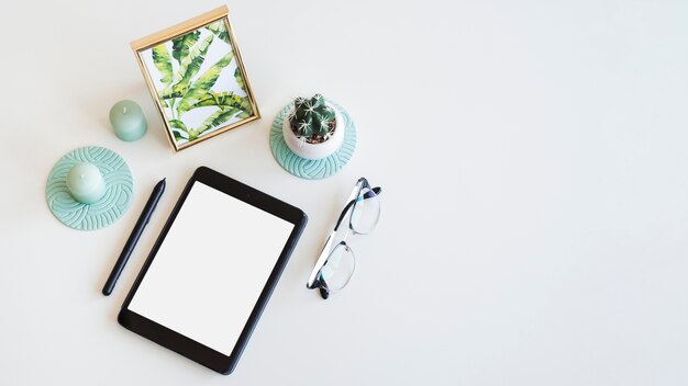 Tafel met tablet in de buurt van fotolijst, kamerplant, pen en bril