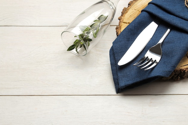 Tafel opstelling. bestek. wijnglas vork, mes in een blauw servet en een houten standaard op een witte houten tafel.
