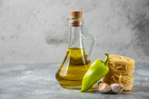 Tagliatelle rauwe pasta nesten, fles olie en groenten op marmeren achtergrond.