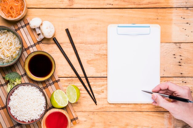 Tai-voedsel met de hand die van een persoon op het klembord met pen op houten bureau schrijven