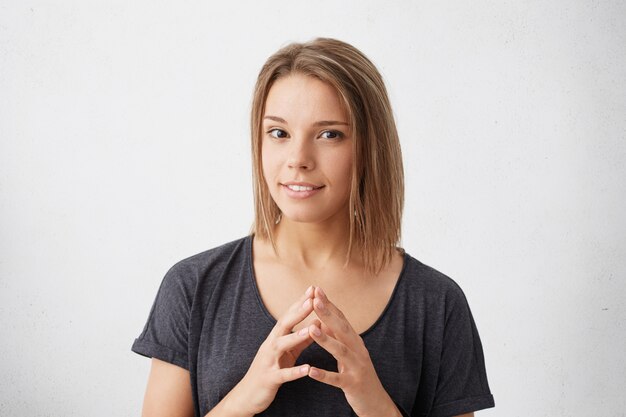 Taille-up portret van een vrouw met afgeknipt haar die haar vingers bij elkaar houdt en kijkt met de een of andere intentie om te beslissen wat te doen.