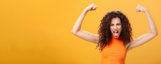 Gratis foto taille-up shot van coole en gedurfde blanke vrouw in oranje top met tatoeage op arm die fronst en fu maakt