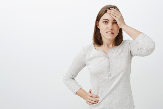 Taille-up shot van slimme creatieve vrouwelijke collega in witte blouse hand in hand op voorhoofd bijten onderlip bezorgd en onrustige geconfronteerd met harde situatie proberen oplossing te vinden over grijze muur