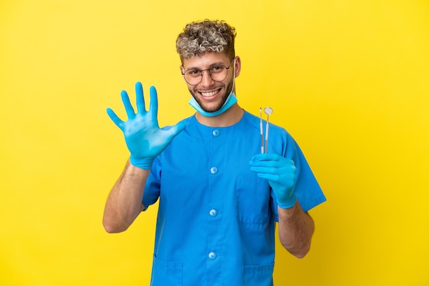 Tandarts blanke man met tools geïsoleerd op gele achtergrond vijf tellen met vingers