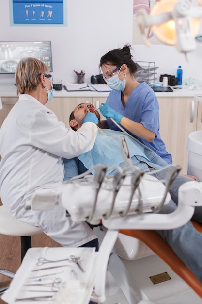Tandartsteam met medische gezichtsmaskers die professionele tandhulpmiddelen gebruiken tijdens stomatologische chirurgie in de bureauruimte van het tandheelkundeziekenhuis. Gespecialiseerde arts werkzaam bij zorgbehandeling