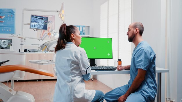 Tandheelkundeteam dat tandenröntgenstraal en groen scherm op monitor op tandartskantoor analyseert. Specialist en verpleegster werken met geïsoleerde mockup-sjabloon en radiografie voor tandverzorging.