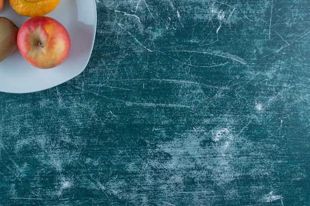 Gratis foto tangerine, kiwi en appels op een bord, op de marmeren tafel.