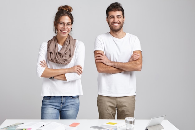 Team van creatieve werkers: mooie lachende vrouw draagt sjaal en grote bril en bebaarde man houdt de handen gevouwen