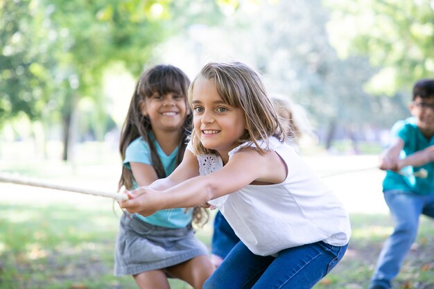 Team van gelukkige kinderen die touw trekken, touwtrekken spelen, genieten van buitenactiviteiten. Groep kinderen plezier in park. Jeugd of teamwerk concept