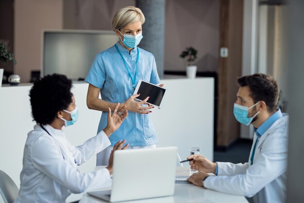 Team van gezondheidswerkers die samenwerken tijdens het gebruik van touchpad tijdens een vergadering in de kliniek