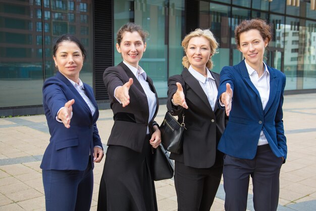 Team van positieve succesvolle ondernemers staan samen in de buurt van kantoorgebouw, bieden handdruk, camera kijken. Vooraanzicht. Samenwerking concept