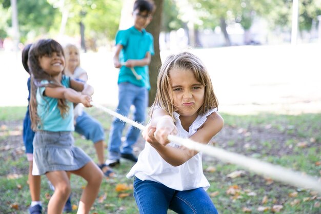 Team van vrolijke kinderen die touw trekken, touwtrekken spelen, genieten van buitenactiviteiten. Groep kinderen plezier in park. Jeugd of teamwerk concept