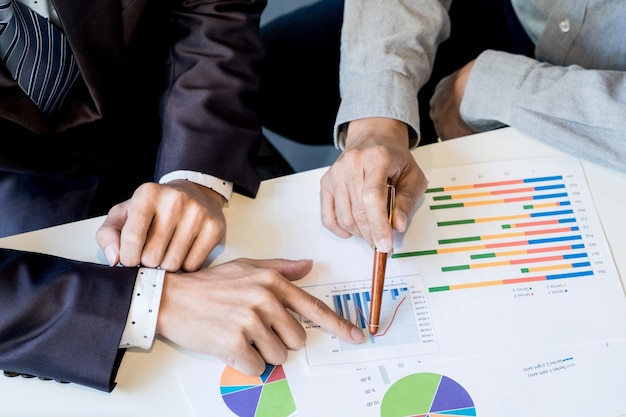 Teamwerkproces. Jonge zakenmanagers die werken met een nieuw opstartproject. Labtop op houten tafel, toetsenbord typen, sms-bericht, grafiekplannen analyseren.