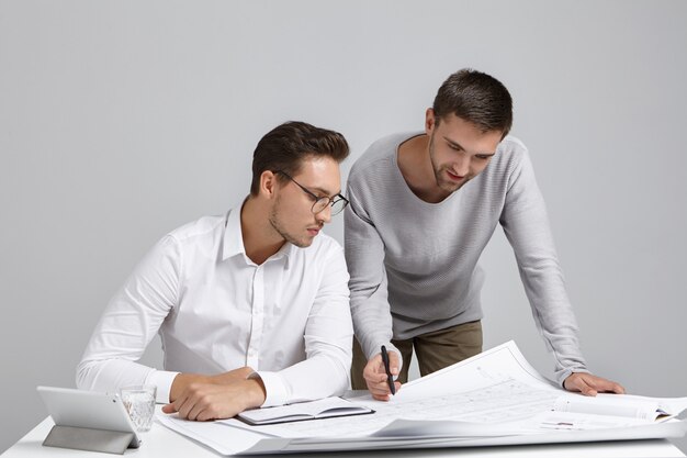 Teamwork, baan en samenwerkingsconcept. Foto van twee enthousiaste getalenteerde jonge bebaarde ingenieurs die samenwerken