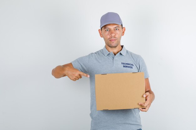 Technische dienst man wijzende vinger op kartonnen doos in grijs t-shirt met pet