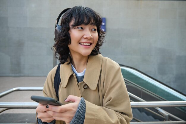 Technologie en mensen jonge Aziatische studente die op straat staat met een koptelefoon luistert naar muziek en sm