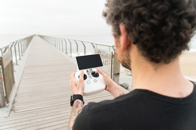 Gratis foto technologisch onderlegde hipster of jonge generatie millennial professionele fotograaf gebruikt afstandsbediening om drone- of quadrocopter-gadget in de lucht te besturen