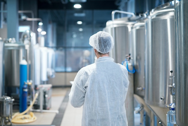 Technoloog die in wit beschermend pak door de productielijn van de voedselfabriek loopt die kwaliteit controleert