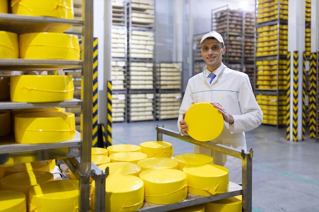 Gratis foto technoloog in een wit gewaad met een gele kaaskop in zijn handen is in de winkel voor de productie van boter en kaas het productieproces in de fabriek van zuivelproducten rekken met kaas