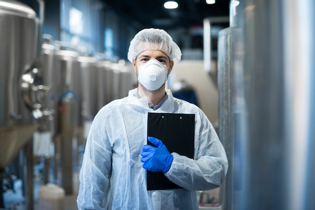 Gratis foto technoloog met beschermend masker en haarnetje staande op de productielijn van de fabriek