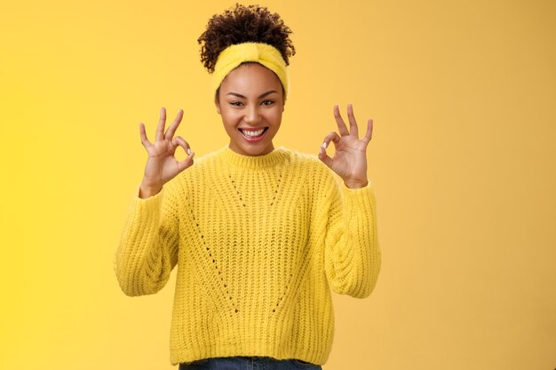 Tel het gedaan. Verzekerde zelfverzekerde afro-amerikaanse vrouw in sweater-hoofdband laat zien oke ok geen zorgen gebaar glimlachend zelfverzekerd plan gaat prima, tevreden goede resultaten, juichende gele achtergrond.