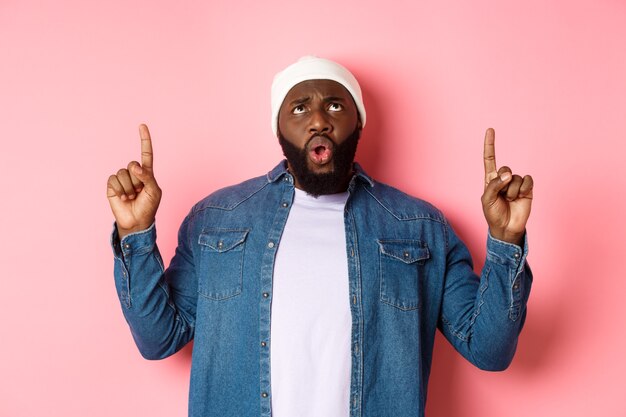 Teleurgestelde afro-amerikaanse man klaagt, kijkt en wijst met de vingers naar slechte promo, ontevreden tegen een roze achtergrond.
