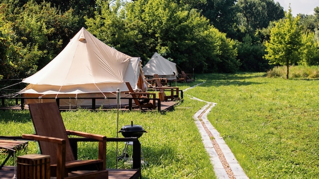 Tenten met houten stoelen en pad ervoor bij glamping. Natuur, groen rondom