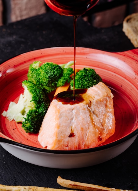 Teriyakisaus toevoegen aan zalmlapje vlees met broccoli in roze kom.