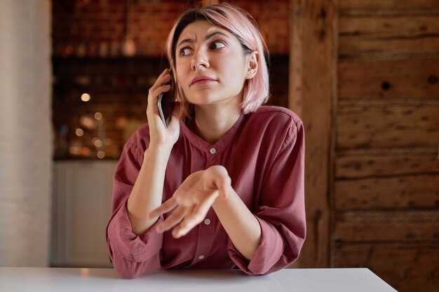 Terloops geklede jonge vrouw met telefoongesprek, emotioneel gebarend van verontwaardiging