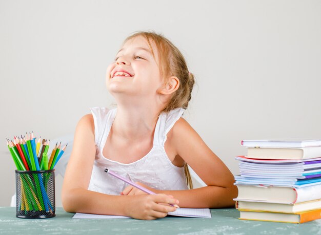 Terug naar schoolconcept met potloden, boeken, voorbeeldenboeken zijaanzicht. klein meisje glimlachend en potlood te houden.