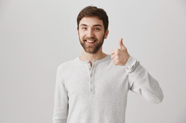 Tevreden, bebaarde mannelijke klant toont goedkeuring met duim omhoog