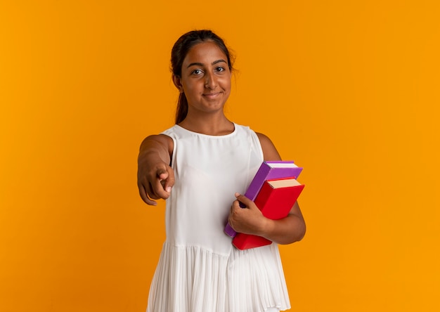 Tevreden jong schoolmeisje dat boeken houdt en u gebaar toont dat op oranje muur wordt geïsoleerd