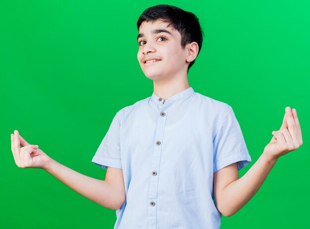 Tevreden jonge blanke jongen die geldgebaar doet dat op groene muur wordt geïsoleerd