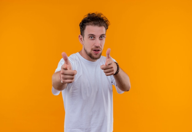 Tevreden jonge kerel die wit t-shirt draagt dat u gebaar op geïsoleerde oranje achtergrond toont