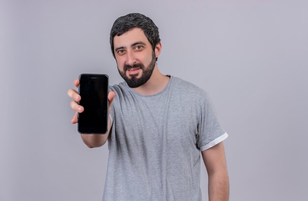 Tevreden jonge knappe man die zich uitstrekt uit mobiele telefoon geïsoleerd op een witte muur