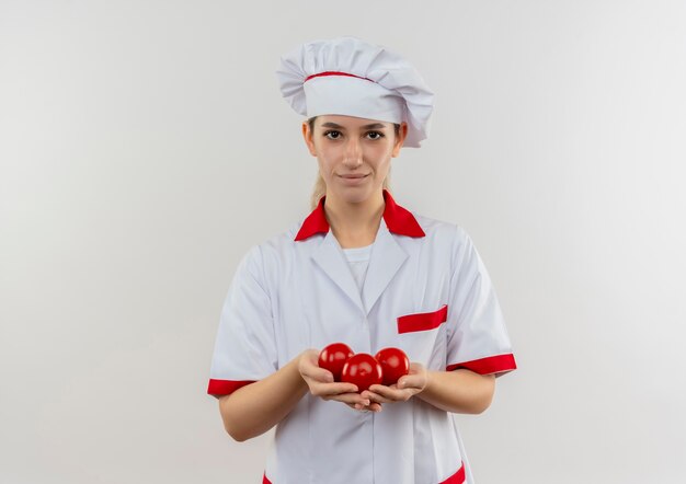 Tevreden jonge mooie kok in tomaten van de chef-kok de eenvormige holding die geïsoleerd op witte ruimte kijken