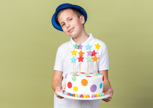Tevreden jonge slavische jongen met blauwe feestmuts met verjaardagstaart geïsoleerd op olijfgroene muur met kopieerruimte
