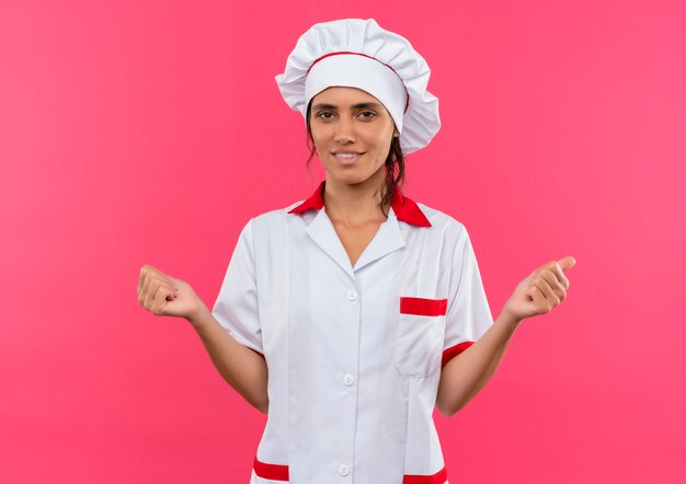 Tevreden jonge vrouwelijke kok die eenvormige chef-kok draagt die ja gebaar met exemplaarruimte toont