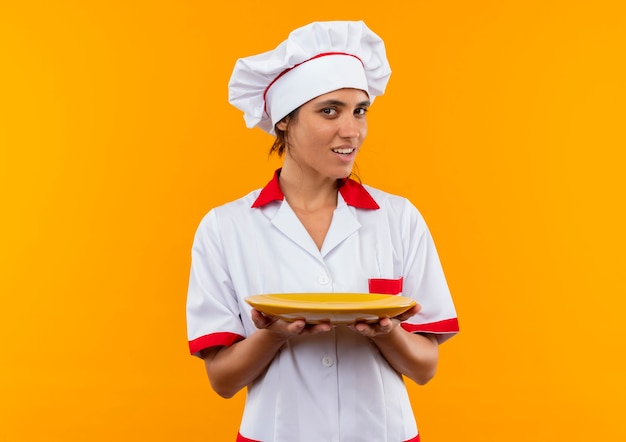 Tevreden jonge vrouwelijke kok die plaat van de chef-kok eenvormige holding met exemplaarruimte draagt
