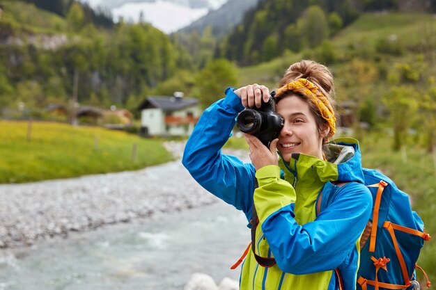 Tevreden jonge vrouwelijke reiziger maakt foto van berg- en rivierlandschap