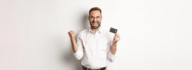 Tevreden knappe man die creditcard toont en zich verheugt over het winnen van iets of het triomferen van staande ov